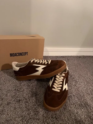 Bruna sneakers från MOACONCEPT - Säljer ett par HELT NYA bruna sneakers från MOACONCEPT. Fick skorna i julklapp men säljer dom nu för att dom ej passade i storlek. Orginal box plus kvitto finns såklart kvar. Skorna har ovandel i mocka och detaljer i skinn, samt en klassisk gummisula. Det är bara att höra av er i DM vid funderingar 🔥 