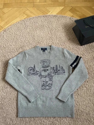 Polo bear Ralph lauren - En snygg stickad polo bear London Ralph lauren sweater.  Den är i storlek 14-16 som på bilden. Sweatern är i mycket bra skick och är redo för att användas. Skriv vid minsta lilla fundering om mått eller annat🌟Sweatern kan skickas snabbt, är i bra skick och lågt pris!