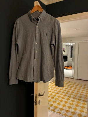 Ljusblå skjorta från Ralph Lauren - Klassisk ljusblå skjorta från Ralph Lauren med button-down krage och broderad logga på bröstet. Skjortan har långa ärmar, knappar framtill och är tillverkad i mjuk bomull. Fin i tyget och inga noppor eller fläckar. 