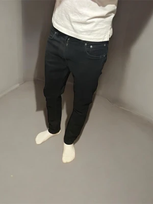 Svarta slim fit nudie jeans - Säljer ett par svarta slim fit jeans från nudie. Modellen är Lean Dean och de är  i storlek 31/30. De har klassisk femficksdesign, raka ben och diskreta sömmar på bakfickorna. Jeansen är i stretchig bomull och har en clean look som passar till allt. Jeansen är i mycket bra skick men har ett litet hål i backfickan (se bild 6) men syns inte när man har på sig dem. Jag är 175cm men sitter lite tajt på mig så passar dig som är ungefär 170cm. Skriv om du har några frågor.