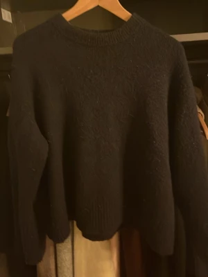 Mörkblå stickad tröja med rund hals - Mysig mörkblå stickad tröja med rund hals och långa ärmar. Tröjan har en enkel och klassisk design med ribbade muddar vid hals, ärmslut och nederkant. Perfekt för kyliga dagar och enkel att matcha med olika outfits.