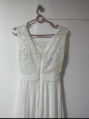 Vet lång spetsklänning - Elegant långklänning i vitt med spetsliv och v-ringad rygg. flytande tyg. Klänningen är ärmlös och har ett markerat midjeband för en snygg siluett. den är bara använd en gång.❤️🌺