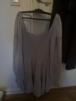 Ljusgrå kortklänning från Bik Bok XS - Supersöt ljusgrå/lila kortklänning från Bik Bok i storlek XS. Klänningen har smockad överdel, vida långa ärmar med broderade detaljer och volang nedtill. Tillverkad i mjukt bomullstyg och perfekt för sommarens alla tillfällen.