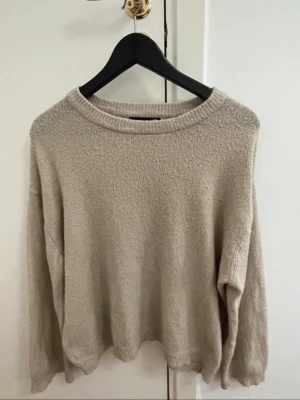 Beige stickad tröja från 157 - Mysig beige stickad tröja från 157 med rund halsringning och ribbade muddar. Perfekt för lager på lager under höst och vinter. Enkel och clean design som passar till allt.