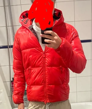 Röd pufferjacka från save the duck.  - Säljer en snygg röd pufferjacka från save the duc k.. Perfekt för kalla dagar och har en cool look med text på insidan av huvan. Nypris 3600.jackan är i bra skick och endast använd i någon månad.