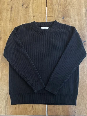 Svart stickad tröja från Maison Margiela - Säljer en svart stickad tröja från Maison Margiela med klassisk ribbad struktur och rund hals. Tröjan har långa ärmar och de ikoniska vita sömmarna i nacken. Perfekt till lager på lager under höst och vinter. Storlek S men passar M-L