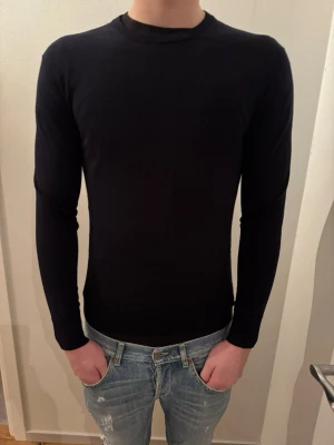 Svart tunn stickad tröja Uniqlo M - Säljer en svart, tunn stickad tröja från Uniqlo i storlek M. Tröjan har rund halsringning och lång ärm, sitter tight och är perfekt för lager på lager. Enkel och stilren design som funkar till det mesta.