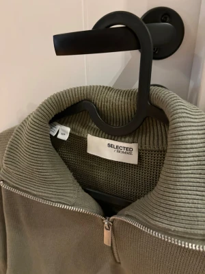 Olivgrön stickad tröja Selected Homme - Säljer en olivgrön stickad tröja från Selected Homme i storlek S. Tröjan har en ribbad krage och half zip-dragkedja framtill. Perfekt för lager på lager och har en avslappnad passform med långa ärmar.