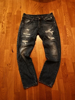 Blå distressed jeans från Fornarina - Säljer ett par blå jeans från Fornarina med slitna detaljer och snyggt tvättad look. Klassisk femficksmodell, orange kontrastsömmar och låg midja. Jeansen har raka ben och är tillverkade i tåligt denimtyg.