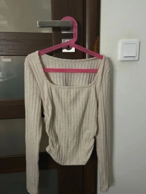 Beige ribbad långärmad topp - Säljer en beige ribbad topp med lång ärm och fyrkantig ringning. Toppen är i mjukt, stretchigt material och har en figurnära passform. Perfekt att styla med jeans eller kjol för en enkel men snygg look.