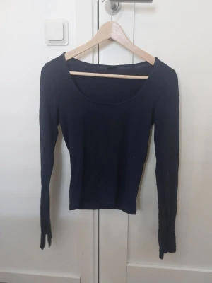 Mörkblå långärmad topp Gina Tricot - En enkel och stilren mörkblå långärmad topp från Gina Tricot. Modellen har en rundad, djup urringning och är figurnära i passformen. Tillverkad i mjukt och stretchigt bomullsmaterial som känns skönt mot huden. Perfekt att matcha med jeans eller kjol.