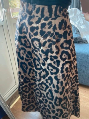 Leopardmönstrad långkjol med slits - Säljer en snygg långkjol med leopardmönster i beige och svart. Kjolen har en hög midja och en slits på sidan som ger en trendig look. Materialet känns mjukt och följsamt, perfekt för dig som vill sticka ut lite extra.