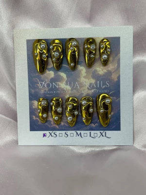 Orphine (XS);Medium Almond - Unika handgjorda press-on naglar i metallic guld med medium lång mandel form och dekorerade med vita pärlor och special effekt av dropp-mönster. Handgjorda och riktigt statement! Perfekt för dig som vill ha något extra till naglarna.XS: 14 mm, 11 mm, 11,5 mm, 10 mm, 8 mm
