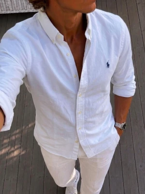 Vit skjorta från Polo Ralph Lauren - Klassisk vit skjorta från Polo Ralph Lauren med button-down krage och broderad logga på bröstet. Skjortan har lång ärm, normal passform och är tillverkad i mjuk bomull. Perfekt till både jeans och chinos för en clean look.