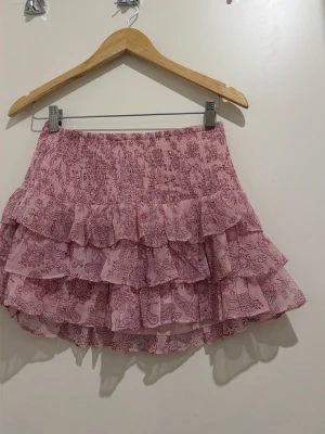 Rosa volangkjol från Gina Tricot - Supersöt rosa kjol från Gina Tricot med volanger och blommigt mönster. Kjolen har en smockad midja som ger en bekväm passform och flera lager volanger för en extra fluffig look. Perfekt för dig som vill ha en lekfull och trendig stil.