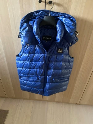 Blå dunväst med huva från BVALDI - Snygg blå dunväst från BVALDI med avtagbar huva och dragkedja framtill, storlek xs 