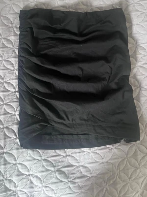Svart tight kortkjol - En svart tight kortkjol med drapering på vänster sida. Kjolen har en rak passform och är perfekt att matcha med olika toppar. .