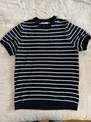 Marinblå randig t-shirt från Zara - Snygg marinblå t-shirt från Zara med vita horisontella ränder. Klassisk rund halsringning och korta ärmar. Perfekt för en avslappnad och stilren look. Tillverkad i mjuk bomull för skön komfort.