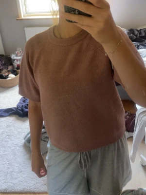 Ljusbrun stickad kortärmad topp - Mysig ljusbrun stickad topp med korta ärmar och rund hals. Enkel och stilren design som passar perfekt till både jeans och kjol. Skön och avslappnad passform, perfekt för vår och sommar.