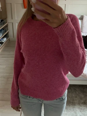 Rosa stickad tröja från veromoda  - Mysig rosa stickad tröja med rund hals och långa ärmar. Tröjan har en enkel, klassisk design med ribbade muddar vid ärmslut och nederkant. Perfekt för dig som gillar en basic men ändå färgglad stil.