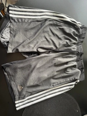 Svarta Adidas shorts med vita ränder - Säljer adidas’s gym shorts storlek M, killmodell. Bra skick! Fickor fram. Gråa med vita ränder!