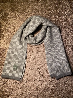 Grå rutig halsduk  - Snygg grå halsduk  med diskret rutmönster. Halsduken är stickad och har en mjuk känsla, perfekt för att hålla värmen under kyliga dagar. Passar till de flesta outfits och ger en exklusiv touch.