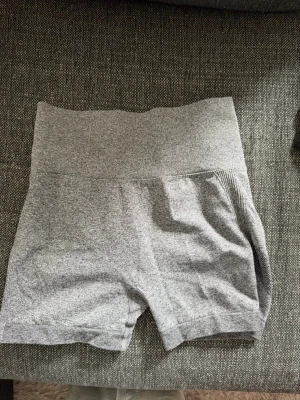 Grå sömlösa träningstights shorts - Gråa sömlösa shorts med hög midja och ribbade detaljer. Perfekta för träning eller chill, med stretchigt material som sitter skönt och formar sig efter kroppen. Kort modell och diskret scrunch baktill för extra passform. Skriv privat för fler bilder eller om du har några frågor💗
