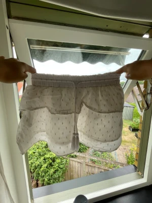 Vit kjol med snörning och prickar - Luftiga vit kjol med elastisk midja och snörning framtill. Kjolen har ett diskret prickigt mönster och är tillverkade i ett tunt, lätt material som passar perfekt för varma dagar.