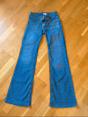 Low Waist Bootcut Jeans Nelly - Blåa low waist bootcut Jeans från Nelly. Dragkedjegylf med knappar framtill, även fickor framtill och baktill.