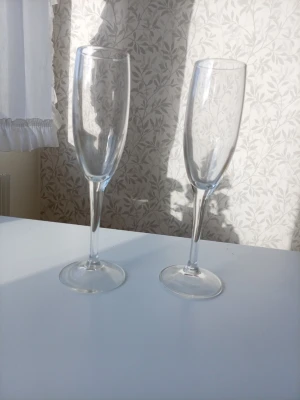 Två champagneglas i klarglas - Säljer två eleganta champagneglas i klarglas med klassisk smal form och lång fot. Perfekta för att fira speciella tillfällen eller bara njuta av bubbel. Stilrena och tidlösa glas som passar till alla typer av drycker med kolsyra.