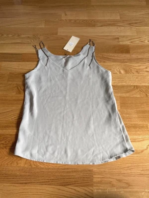 Topp ny stl L - Helt ny turkos topp från Vera&Lucy i storlek L.  Blusmaterial, har kedjor som axelband.  Ena kedjan ser lite mörkare ut än de andra, men den köptes så (se sista bilden).  Köptes för 115 kr. 