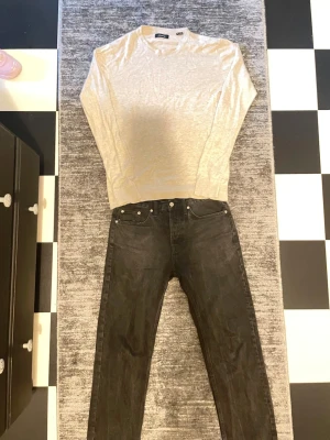 Beige stickad tröja med rund hals - Snygg beige stickad tröja med rund halsringning och långa ärmar. Tröjan har ribbade muddar vid ärmslut och nederkant. Enkel och stilren design som passar till det mesta. Materialet ser ut att vara mjukt och tunt, perfekt för lager på lager.