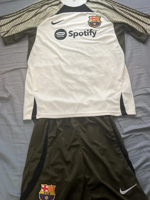 Barcelona Nike matchställ oliv/vit - Säljer ett FC Barcelona matchställ i olivgrönt och vitt, det är storlek M men passar som S också. Tröjan har klubbmärke, Nike-logga och Spotify som sponsor framtill. Setet består av en kortärmad tröja och shorts i funktionsmaterial, perfekt för fotbollsträning eller match. Pris kan diskuteras vid snabb affär. 