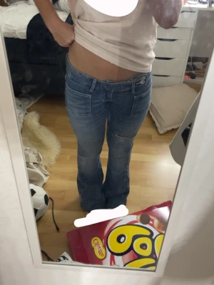 Blå bootcut jeans med slitningar - Säljer ett par blå bootcut jeans med slitningar på låren och knäna. Jeansen har låg midja, klassiska fickor. Knappt använda, det ända är att det är uppsydda till mig som är typ 156 men fortfarande lite långa för mig, går säkert att spreta upp eller något liknande. 