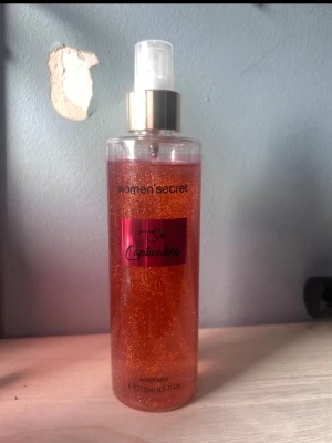 Women’secret So Captivating Body Mist - Fräsch body mist från Women’secret i doften So Captivating. Flaskan är genomskinlig med guldglittrande vätska och har en rosa etikett samt guldfärgad spraypump. Rymmer 250 ml och ger en lyxig känsla med sin skimrande look.