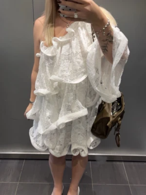 Vit spetsklänning med volang  - Supersnygg vit kort klänning från NA-KD i spets med volangdetaljer och oneshoulder-design. Klänningen har en luftig och unik look med lager av spets och stora volanger. Använd 1 gång, så som gott som ny :)
