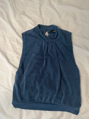 Blå ärmlös topp  - Snygg blå ärmlös topp och lätt rynk vid halsringningen. Toppen har en relaxed passform. Tillverkad i mjukt material som känns skönt mot huden.