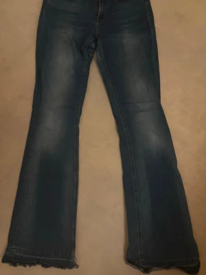Blå bootcut jeans med rå kant - Snygga blå bootcut jeans med rå, fransig kant längst ner på benen. Jeansen har klassisk femficksdesign och en lätt tvättad look med slitningar. Perfekta för dig som gillar en avslappnad men trendig stil. Är inte helt säker på storleken eftersom lappen är avskuren, men jag antar det skulle passa L eller M. Den har lite slitningar längst ner som kan fixas. 