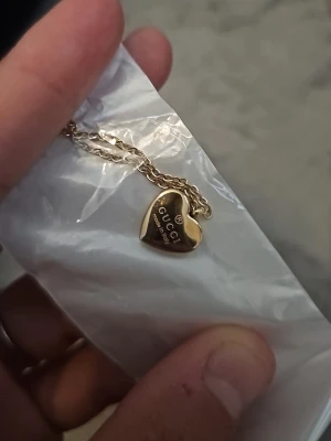 Guldfärgat hjärthalsband  - Säljer ett snyggt halsband i guldfärg med ett hjärtformat hänge. Kedjan är tunn och elegant, och hjärtat har loggan ingraverad på framsidan. Perfekt accessoar för dig som gillar exklusiva detaljer och stilren design.