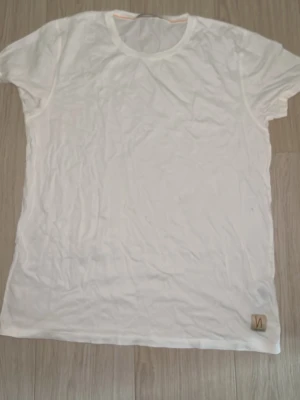 Nudie Jeans Co – Vit T-shirt (Strl M - Vit t-shirt från Nudie Jeans Co Klassisk och mjuk vit t-shirt från det svenska märket Nudie Jeans Co. T-shirten har märkets karaktäristiska orangea söm i nacken och en liten diskret logga nedtill i hörnet. Perfekt basplagg till garderoben! Jag tar inte bilder så bra men kontakta mig om  intresse 
