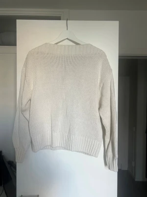 Vit oversized stickad tröja - Säljer en vit oversized stickad tröja med bred ribbad mudd vid ärmslut och nederkant. Tröjan har en avslappnad passform och är perfekt för lager på lager. Enkel och stilren design som passar till det mesta.