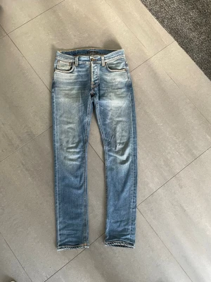 Nudie jeans - Snygga blå slim fit jeans med tvättade detaljer på låren och knäna. Klassisk femficksmodell med normal midja. Perfekta för en avslappnad och trendig look.