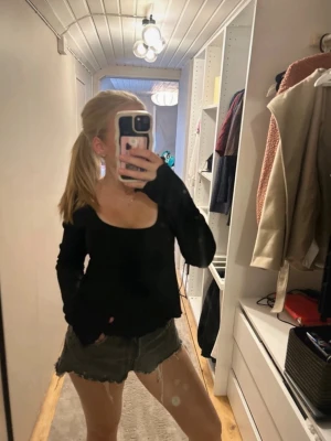 Svart långärmad topp med djup urringning - Trendig svart topp med lång ärm och djup urringning. Modellen är figurnära och har en enkel, stilren design som passar till många outfits. Tyget ser mjukt och stretchigt ut för extra komfort.