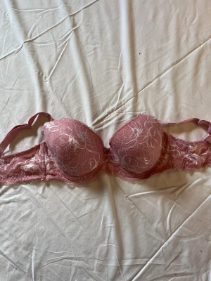 Rosa spets-bh  - Söt rosa bh med vadderade kupor och vacker spetsdetalj över hela bh:n. Justerbara axelband och blommigt spetsmönster ger en romantisk känsla. 