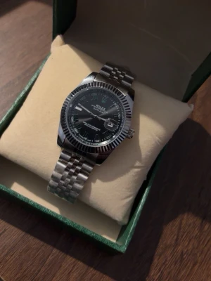 Klocka - Snygg klocka med klassisk silverlänk och svart urtavla. Klockan har räfflad bezel och datumvisning. Perfekt accessoar för dig som gillar stilrena detaljer och exklusiv känsla.