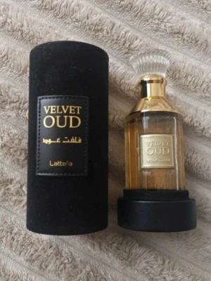 Lattafa Velvet Oud parfym - Lattafa Velvet Oud är en lyxig parfym i en elegant glasflaska med gulddetaljer och genomskinlig kork. Flaskan kommer i en svart cylinderformad sammetsbox med guldfärgad text. Doften har orientaliska och träiga inslag.