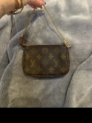 Louis Vuitton monogram kuvertväska. Priset kan diskuteras. - Snygg brun kuvertväska från Louis Vuitton med klassiskt monogrammönster och guldfärgad kedja. Väskan har dragkedja upptill och är perfekt för att bära det viktigaste. Tillverkad i canvas med detaljer i läder.