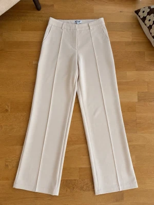Beiga kostymbyxor - Snygga beiga kostymbyxor med raka, vida ben och pressveck framtill. Byxorna har hög midja och diskreta sidofickor. Perfekta för en avslappnad men stilren look. Tillverkade i ett lätt och luftigt material