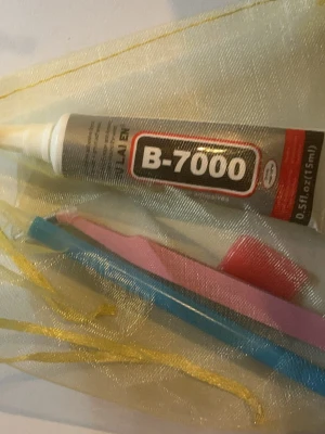 B-7000 lim och verktyg - Säljer ett set med B-7000 lim (15 ml) och två verktyg, en blå pincett och ett rosa verktyg. Perfekt för pyssel, DIY eller småfix. Allt ligger i en genomskinlig påse med gulddetaljer.