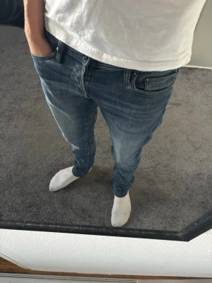 Jack & Jones jeans - Säljer ett par blå slim fit jeans med klassisk femficksdesign och normal midja. Jeansen har en snygg tvättad look och raka ben. Perfekta till vardagsstilen och passar till det mesta. Materialet är troligtvis bomull med lite stretch för extra komfort.
